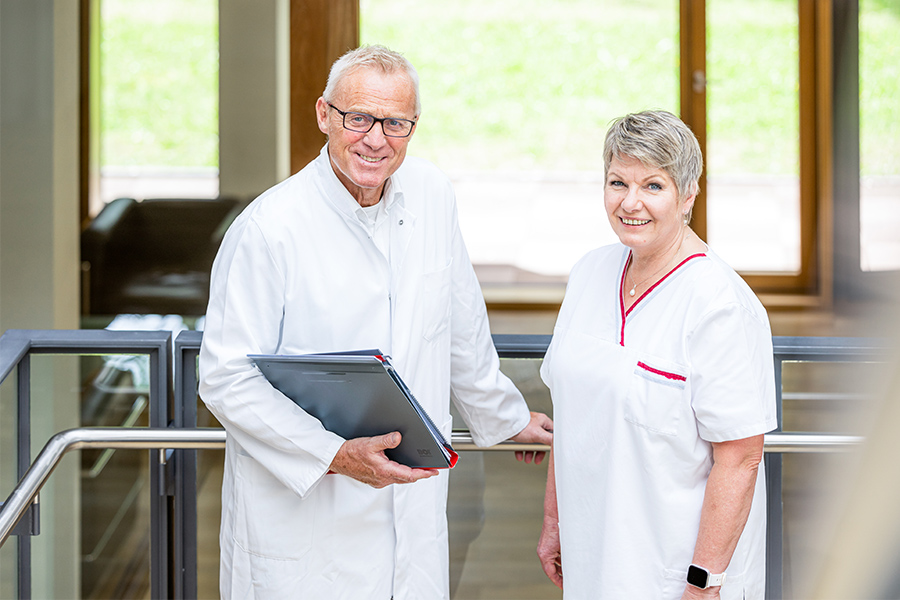 Ein Arzt und eine Pflegerin stehen nebeneinander und lächeln in die Kamera. Ein Arzt und eine Pflegerin stehen nebeneinander und lächeln in die Kamera.