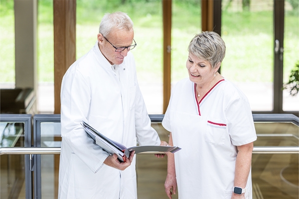 Arzt und Pflegekraft stehen auf dem Flur und schauen gemeinsam in eine Patientenakte Arzt und Pflegekraft stehen auf dem Flur und schauen gemeinsam in eine Patientenakte