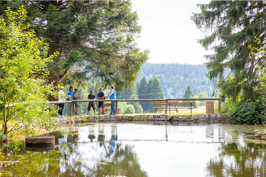 Mehrere Männer mit Walking-Stöcken machen eine Pause an einem Teich im Wald. Mehrere Männer mit Walking-Stöcken machen eine Pause an einem Teich im Wald.