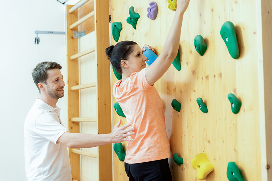 Ein Therapeut unterstützt eine Patientin beim Training an der Kletterwand.
