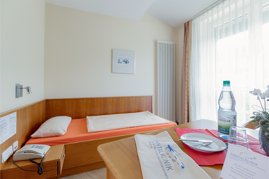 Ein beispielhaftes Patientenzimmer mit gedecktem Tisch im Vordergrund und Bett im Hintergrund.